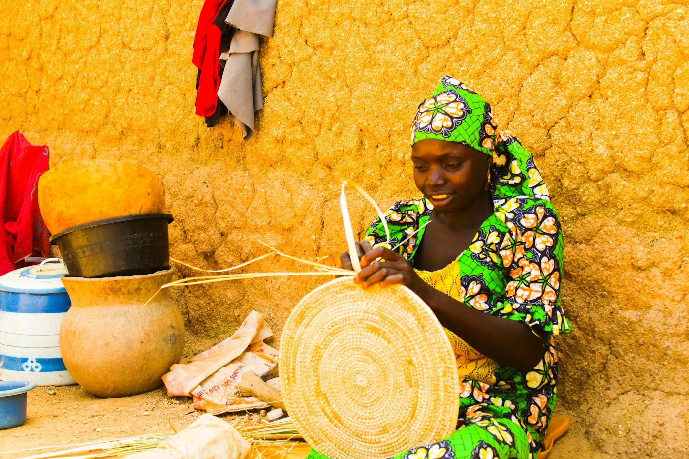 A woman smiling as she weaves a round basket by hand