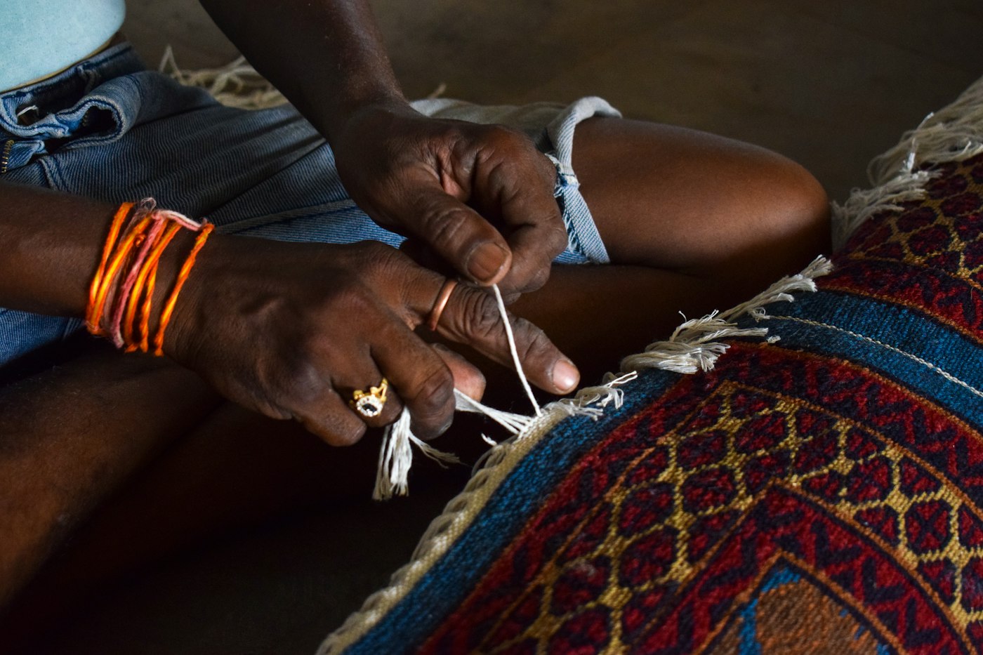 Hands tying the fringe of a colourful woven rug