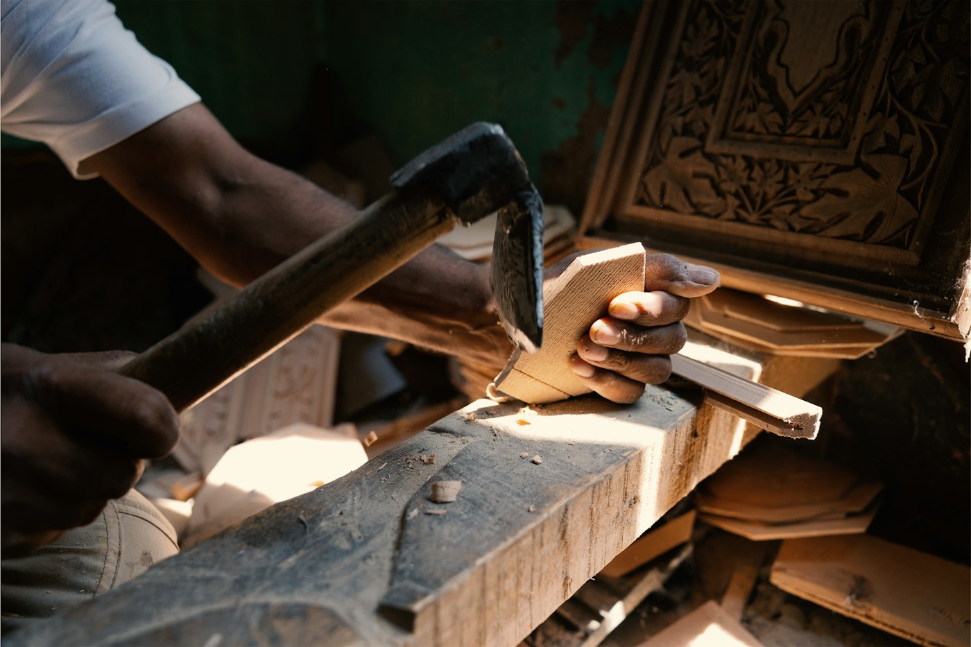 Hands carving a wooden panel with a hammer and chisel